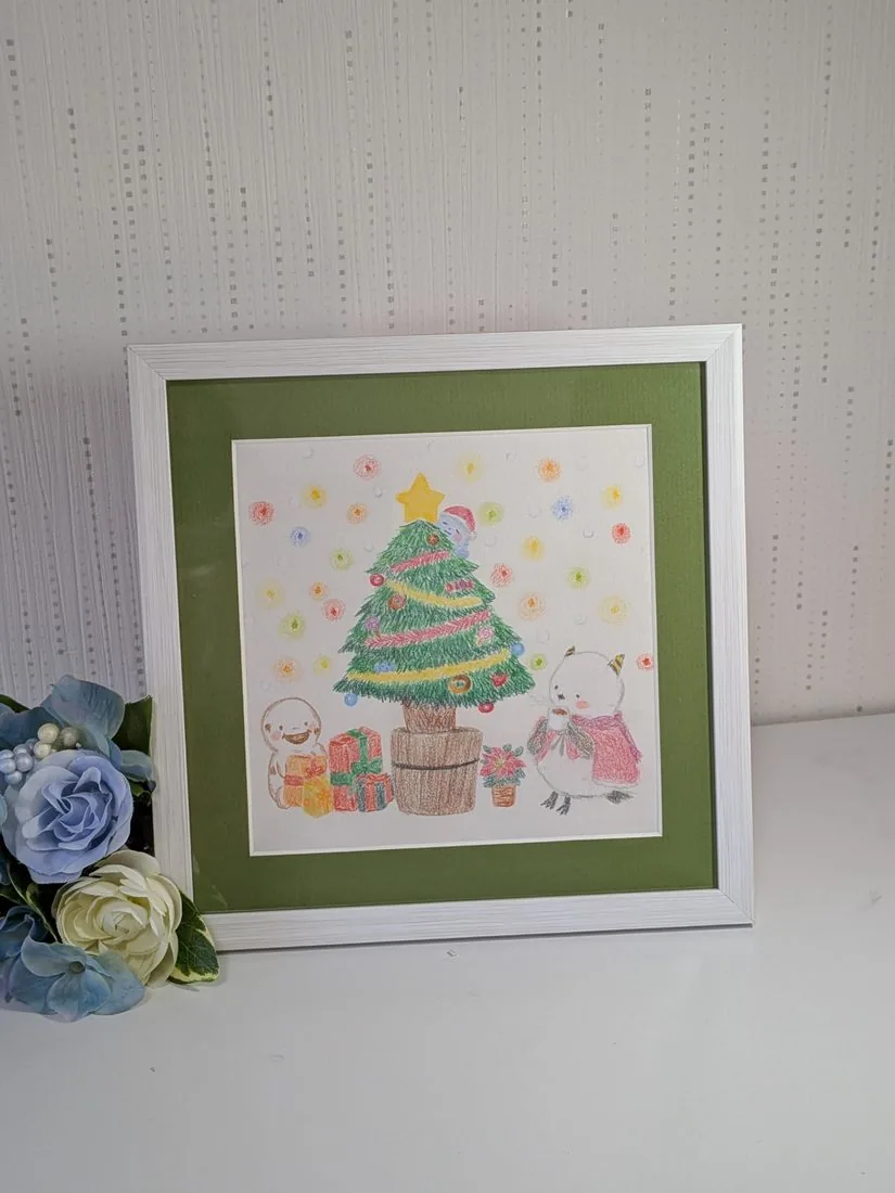 クリスマスツリーとキャラクターの絵を額に入れた様子